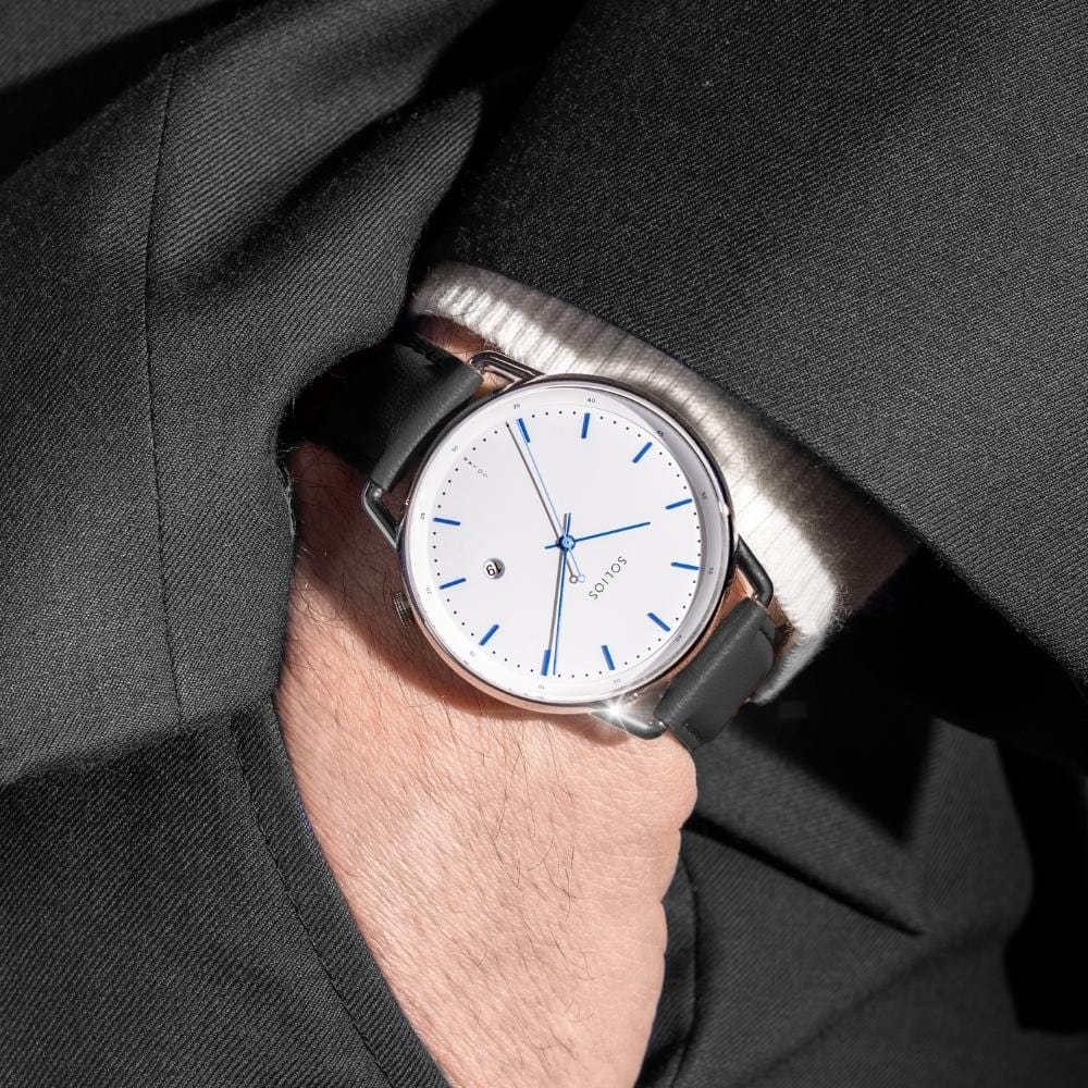 Man wearing the Solios Solar Curve under a navy suit cuff, white dial, silver case, black vegan leather strap