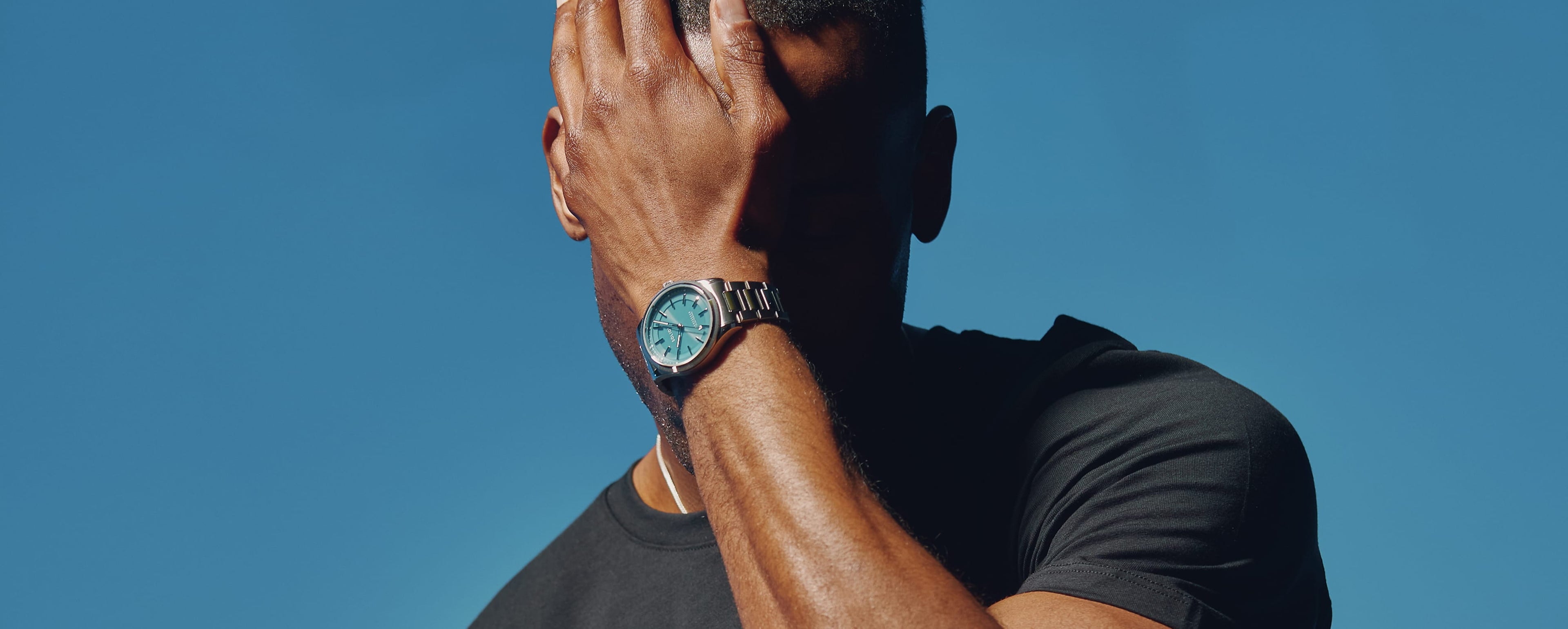 Man wearing the Blue Dial Sunseeker Solar Watch with his hand hiding his face on light blue background