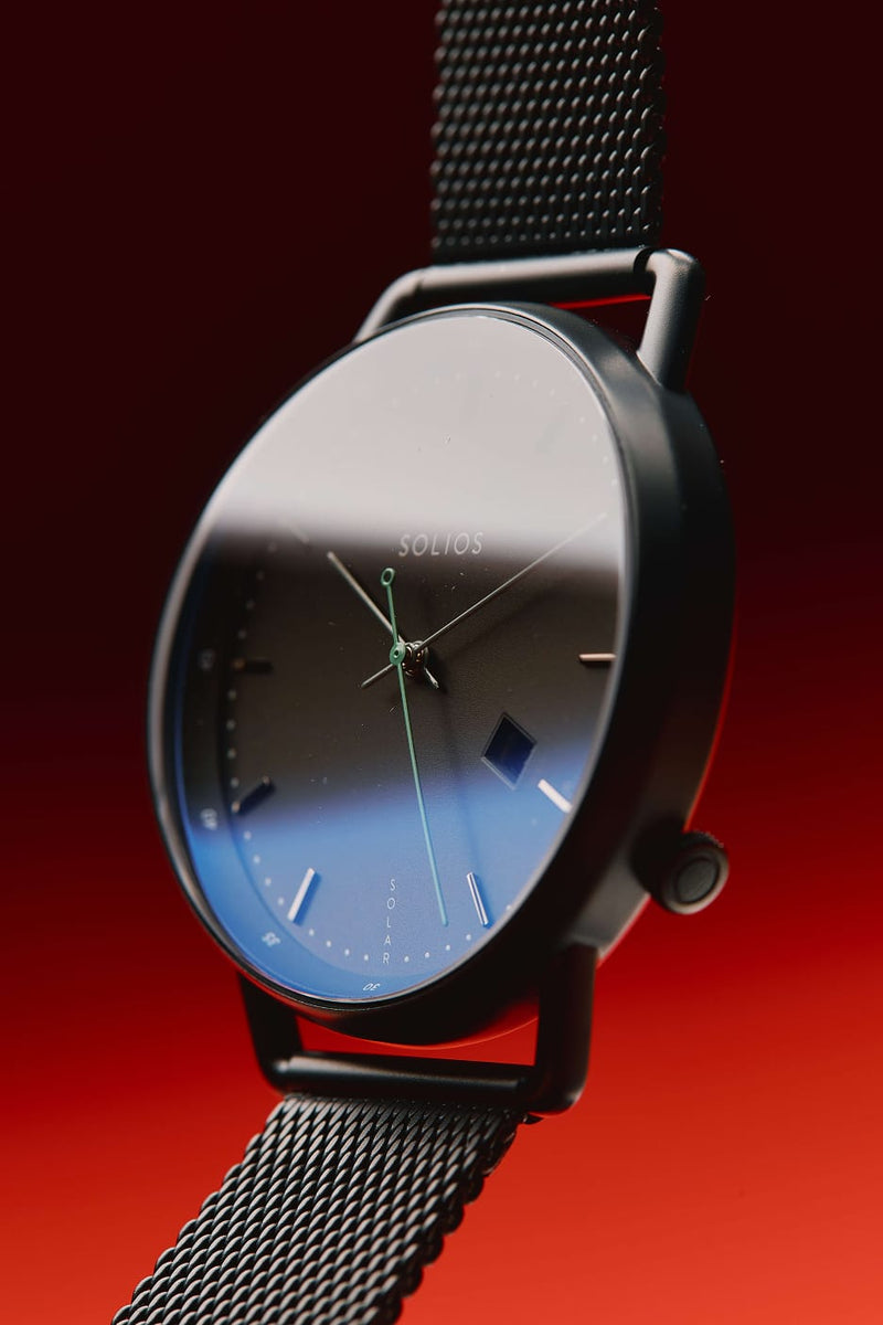 Solios Curve watch, black dial and black case on a mesh strap, on a red background