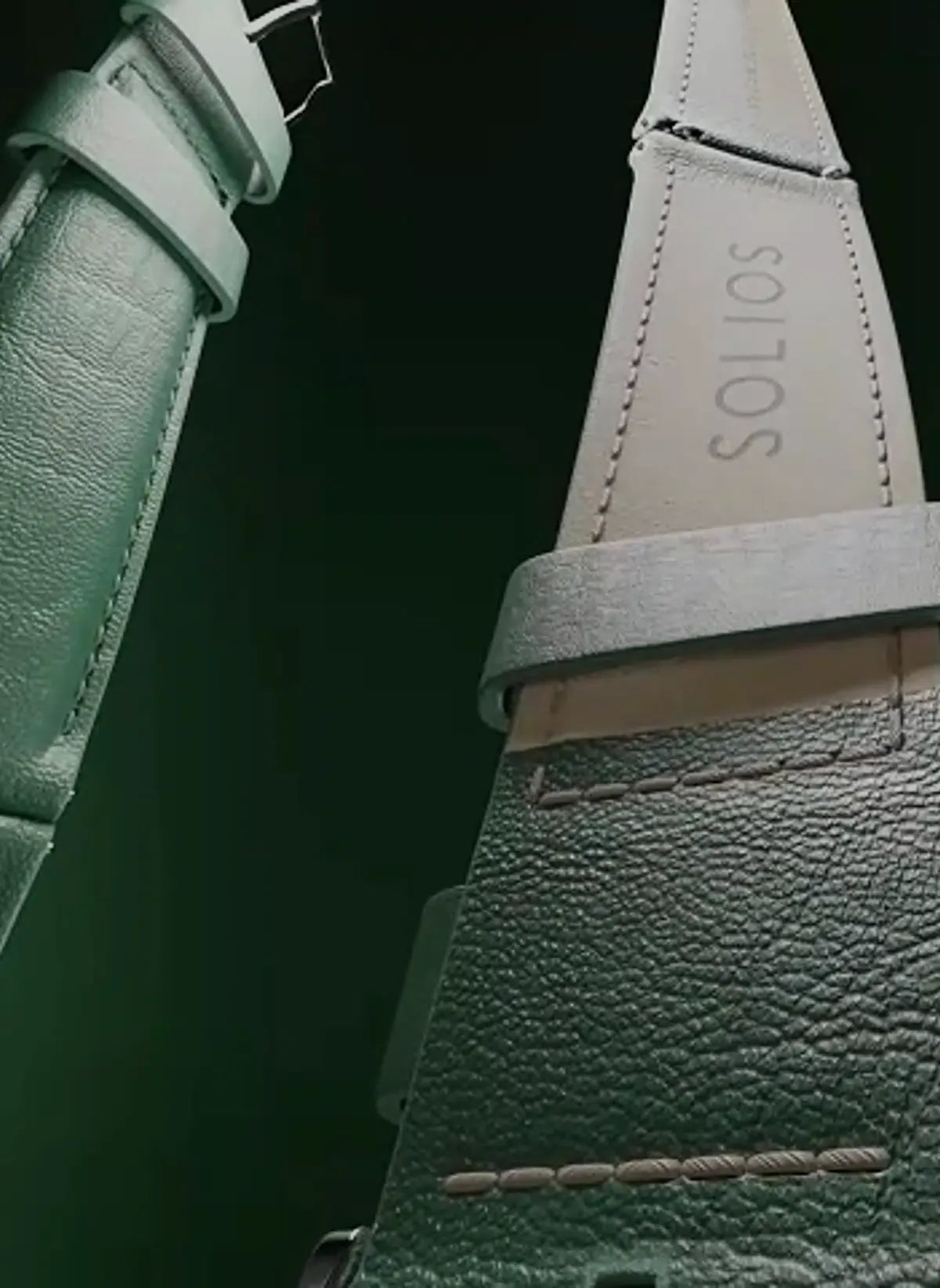 Close-up of a textured Solios vegan leather strap, PU-free, in a muted green color, showing a buckle on one end and the brand name 'SOLIOS' debossed on the insole of another strap section.