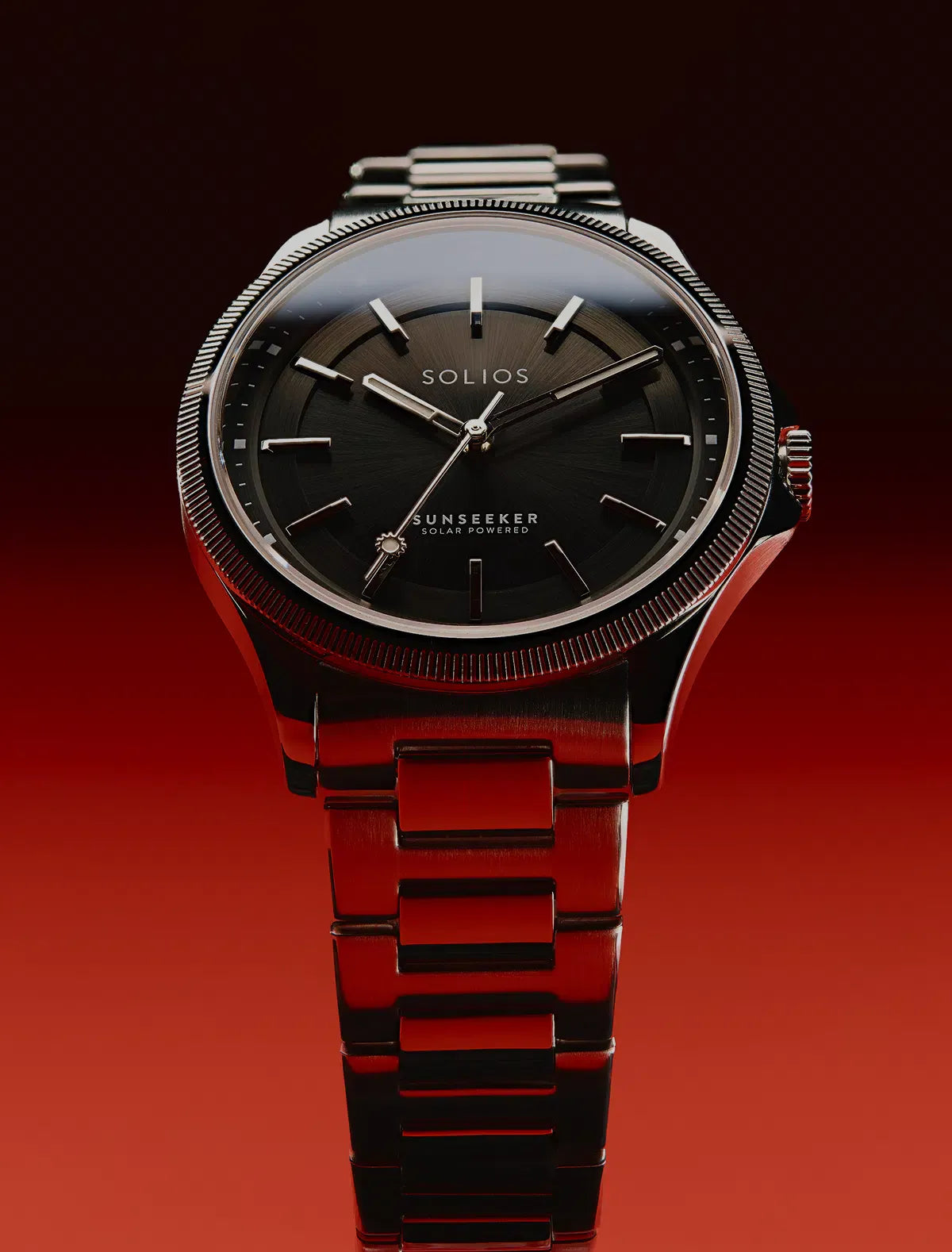 A SOLIOS Sunseeker solar men's watch with a black dial and a dark metallic link bracelet, set against a dark red gradient background.