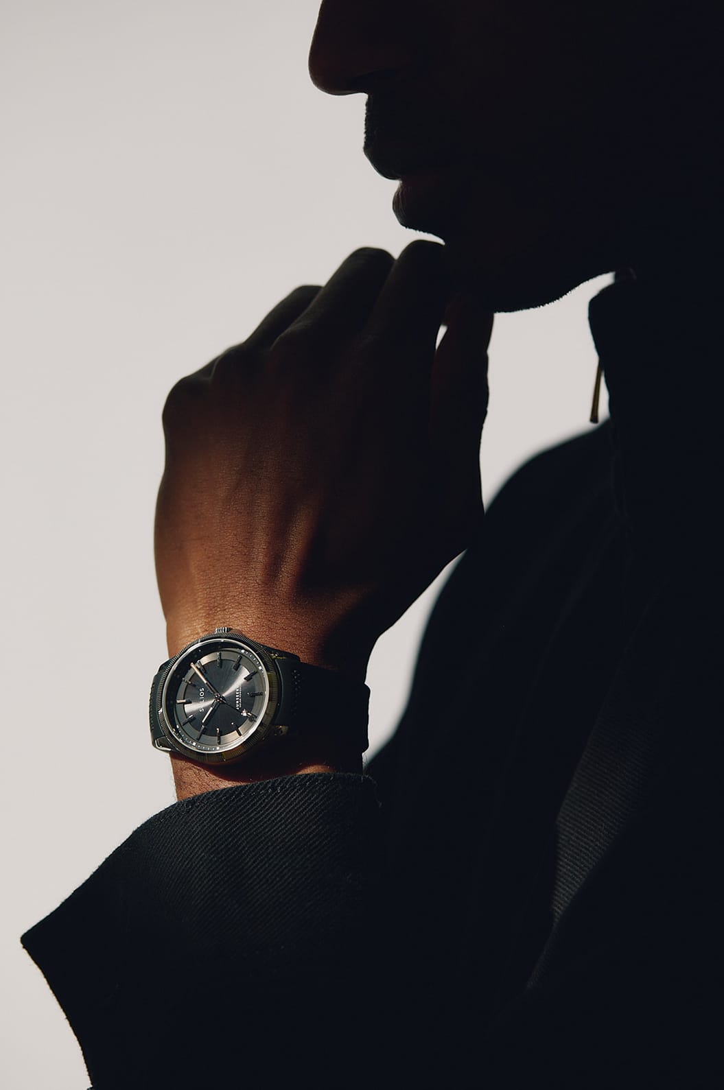 A close-up silhouette of a man wearing a Solios Sunseeker Solar Watch with a black dial and silver-toned case, set against a high-contrast light background.
