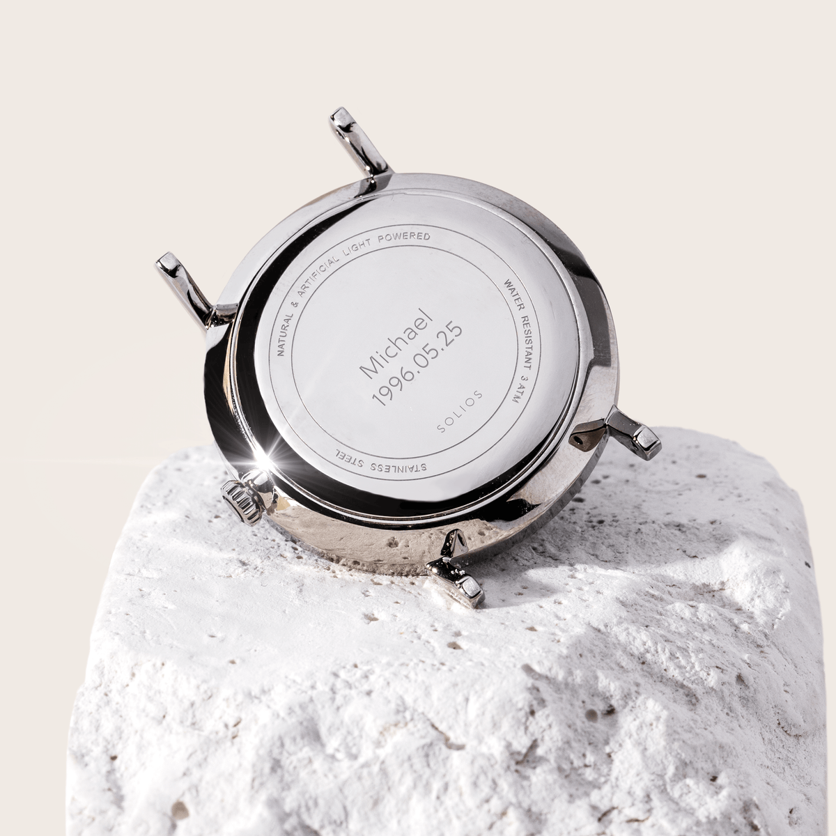 Solios watch caseback resting on a white stone, engraved with a name and date as a custom engraving example